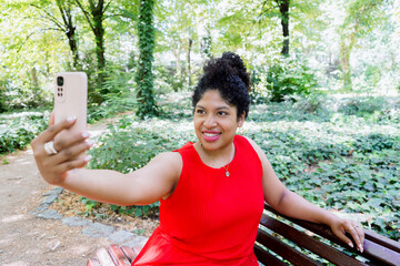 young beautiful and happy black afro American woman in red dress taking selfie photo with mobile...