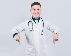 Young doctor pointing a promotion down. Happy doctor pointing fingers down. Latin doctor pointing down an isolated advertising space