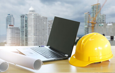 Yellow engineer hat on the table There is a laptop and construction plans. ,under the concept of construction and design