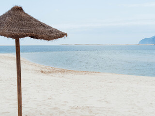 Straw umbrella on empty seaside beach. Beach holiday concept.