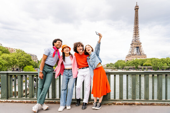 Group of young happy friends visiting Paris and Eiffel Tower - Multiethnic teens bonding outdoors and having fun sightseeing the city