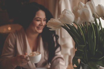 Beautiful woman drressed biege elegant suit sit in cafe and drink the cup of coffee. The plus size...