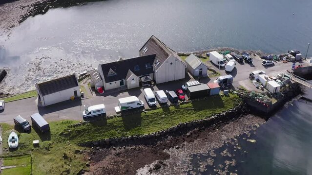 Dynamic drone shot of the community centre on the Isle of Scalpay, an island near the Isles of Harris and Lewis on the Outer Hebrides of Scotland. The Minch sea is visible in the background.
