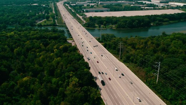 Beautiful aerial in the summer over Highway Interstate I 90 and Fox River. Semi trucks, dryvans, reefers, cars, busses driving on jane addams memorial tollway. Utility poles. Elgin Illinois, USA