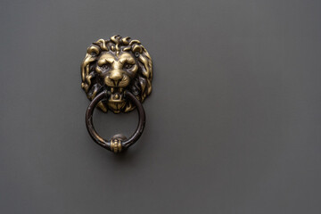 Old brass lion head door knocker on a grey door. Grey background.