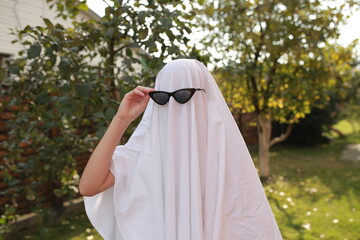 Concept of Halloween, Ghost with sunglasses. a girl in the role of a ghost runs on green grass....