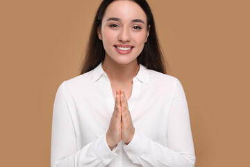 Thank you gesture. Beautiful grateful woman with hands clasped together on brown background