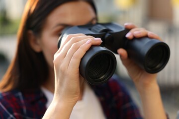 Concept of private life. Curious young woman with binoculars spying on neighbours outdoors, closeup