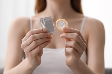 Woman holding unwrapped condom indoors, closeup. Safe sex - obrazy, fototapety, plakaty