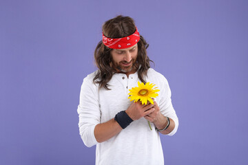 Stylish hippie man with sunflower on violet background