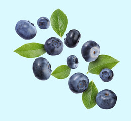 Many ripe blueberries and green leaves falling on light blue background