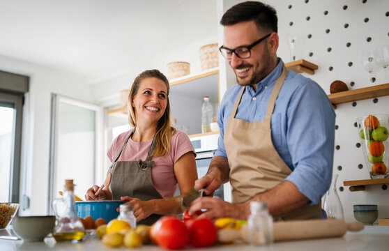 Young Happy Couple Is Enjoying And Preparing Healthy Meal In Their Kitchen Together