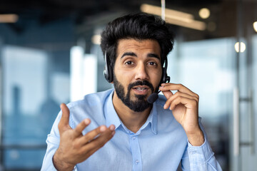 Close-up photo of an Indian male businessman sitting in a headset in the office and communicating...