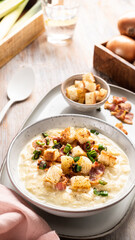 bowl of hot leek cheese soup with croutons and bacon on a wooden table.
