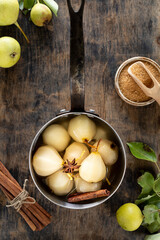 STEWED PEARS. pot of sweet pears stewed in syrup or white wine on a green wooden table.