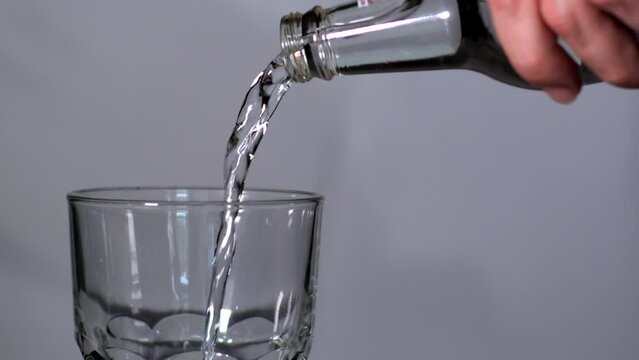 Water Poring Into Glass. Water Bubbles Closeup. Water Drops From Transparent Bottle on grey Background in Slow Motion 