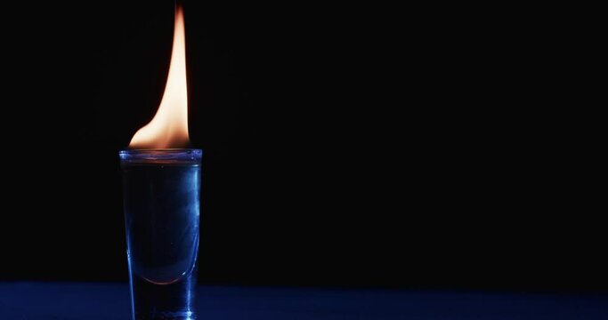 Video of lit alcohol in glass with yellow fire flames and copy space on black background