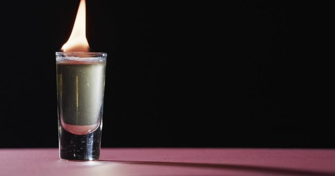 Video of lit alcohol in glass with yellow fire flames and copy space on black background