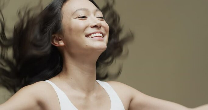 Happy asian woman with dark hair on beige background with copy space, slow motion