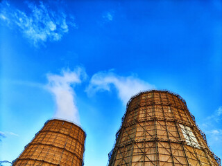 CHP cooling towers from which smoke is coming out against blue sky. A large pipe of a thermal power...