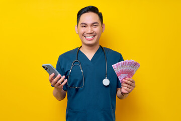 Portrait of a smiling young Asian male doctor or nurse wearing blue uniform holding cash money and...