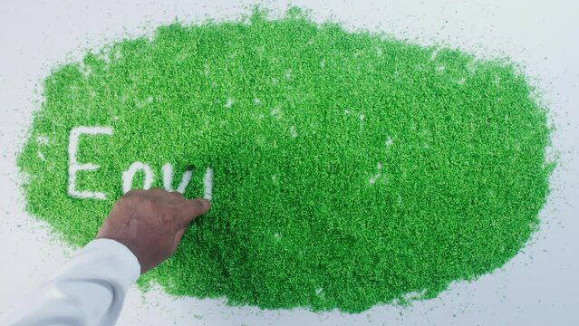 A hand of a person in a shirt writing on green sand words Environment