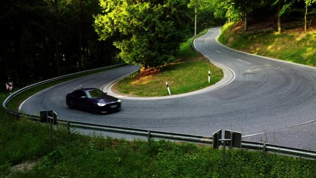 drone shot of a car driving dynamically through a sharp turn in a green forest in summer