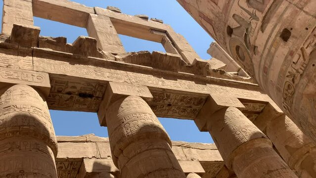 Karnac, Egypt.  Two tiers of ancient temple columns with engraved and painted heiroglyphics on sunny day. Pan out.