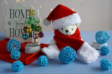 interior decoration for winter holidays with a white teddy bear in a red hat and a Santa Claus scarf with a glass decorated Christmas tree with colorful balloons and a sign with the inscription for