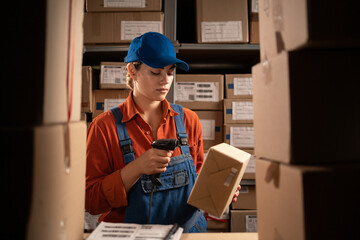 Warehouse storage technologies concept. Storage of goods. Storekeeper job. Woman in overalls reads a barcode on box.