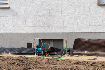Tap for water near the wall of a house under construction with a green hose.
