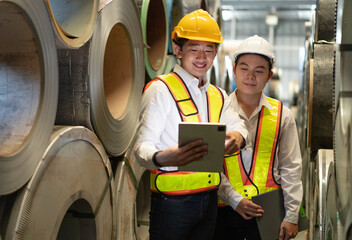 Industrial engineer and colleague wear safety helmet examining production in heavy steel engineering factory. Professional inspector and foreman worker inspecting material in manufacturing facility.