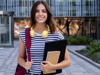 Portrait of student girl with folder in a campus looking at camera smiling. Happy student 