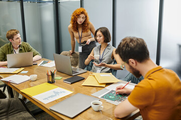 coworking office, laptops, documents, redhead entrepreneur near creative team working on startup