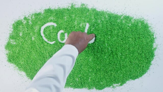 A hand of a person in a shirt writing on green sand words Carbon footprint