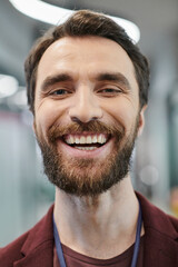 Fototapeta premium portrait of excited bearded businessman with radiant smile looking at camera in contemporary office