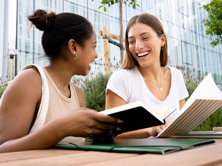 Two teenage smiling diverse female students doing schoolwork together on a campus. student girls