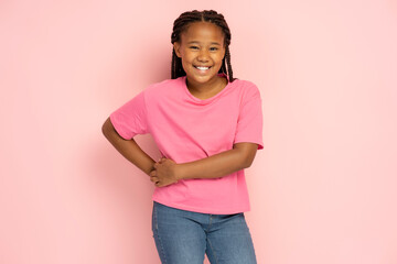 Portrait of cute smiling African American girl with stylish hair wearing pink casual t shirt looking at camera isolated on pink background