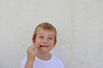 A   joyful boy bites off breadsticks against the background of a concrete wall. Happy childhood.