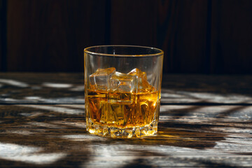 A glass of whiskey and ice stands on an old wooden table