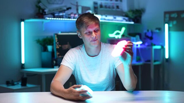 Portrait of vlogger male talking, looking, examining, testing out professional new mini LED lamps sitting at desk on background of desktop computer with neon light background. Shooting in slow motion.