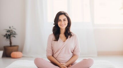 Portrait of a happy pregnant woman sitting cross legged at home. Expecting mother with folded legs stroking her belly smiling and looking at the camera on a sunny day. Young pregnant woman with smile.