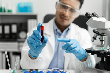 Doctor taking a blood sample tube from a rack with machines of analysis in the lab background,...