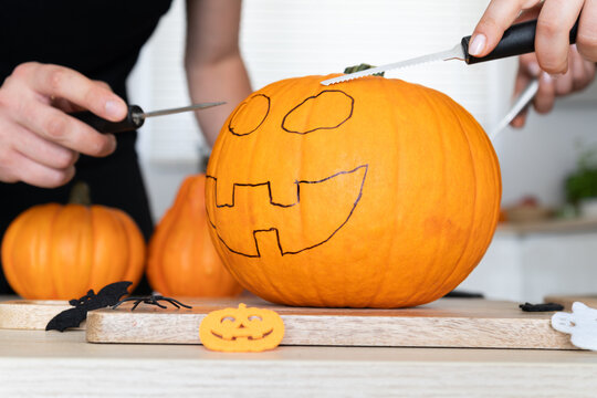 Couple preparing to carve Halloween pumpkins, spooky Jack-o'-lantern cut out. Man and woman holding carving tools, knives, carvers, saw knife blades. Approaching pumpkin with face design painted on it
