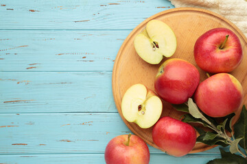 Ripe red apples with green leaves on cutting board on blue wooden background.