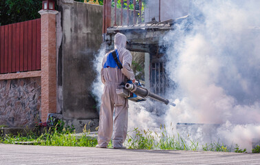 Healthcare worker in protective clothing on street is spraying chemical to eliminate mosquitoes in...