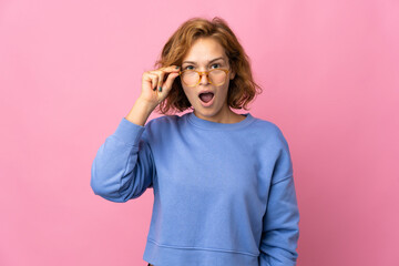 Young Georgian woman isolated on pink background with glasses and surprised