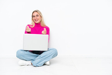 Young caucasian woman with laptop sitting on the floor making money gesture