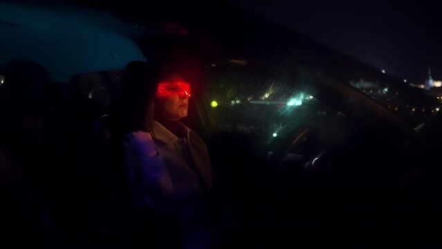 Young beautiful woman uses virtual reality glasses in the car during late rainy night