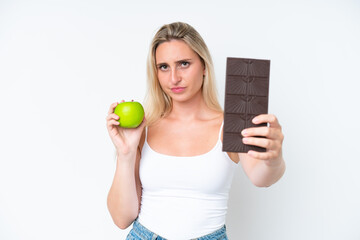 Young caucasian woman isolated on white background taking a chocolate tablet in one hand and an...